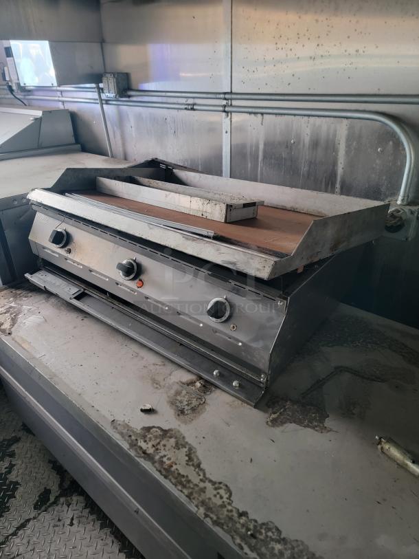 Heavy-duty griddle inside a 2020 24' Diamond Cargo mobile kitchen, showing signs of use and in need of cleaning.