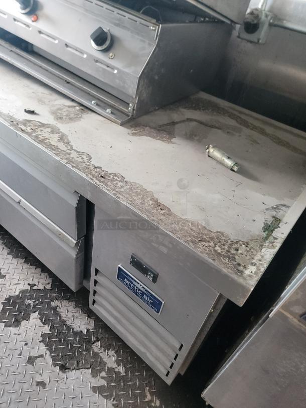 Mobile kitchen interior showing a stainless steel counter, Arctic Air refrigeration unit label, and signs of wear needing cleaning.