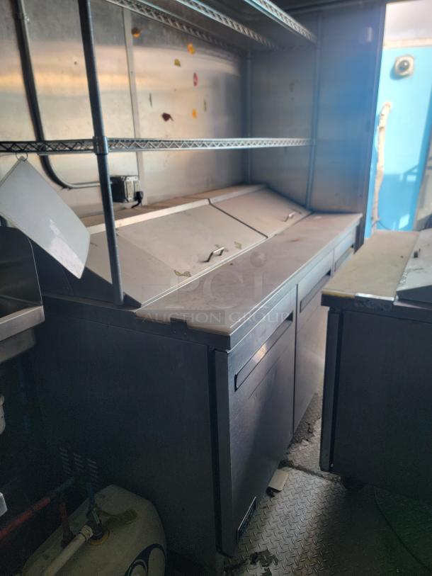 Diamond Cargo mobile kitchen interior with stainless steel prep station, shelving, Arctic Air freezer, and signs of storage dust.