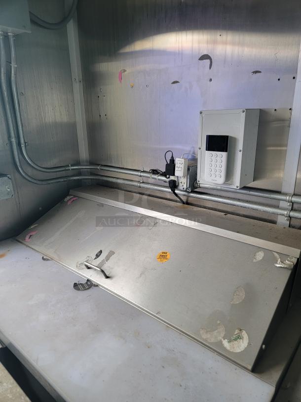 Interior of 2020 Diamond Cargo mobile kitchen. Visible are stainless steel surfaces needing cleaning, a keypad control box, and labeled outlets.