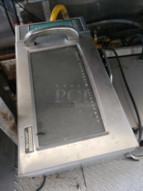 Sharp commercial microwave oven in used condition, showing surface wear. Stainless steel exterior with visible control panel.
