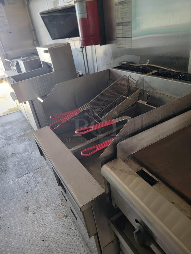 Diamond Cargo 8.5x24 mobile kitchen interior with dual deep fryers, large flat-top griddle, and stainless exhaust hood. Needs cleaning.