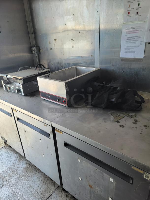 2019 Diamond Cargo 8.5x24 mobile kitchen interior, showing Arctic Air fridge, dual fryers, griddle, and stainless hood. Needs cleaning.
