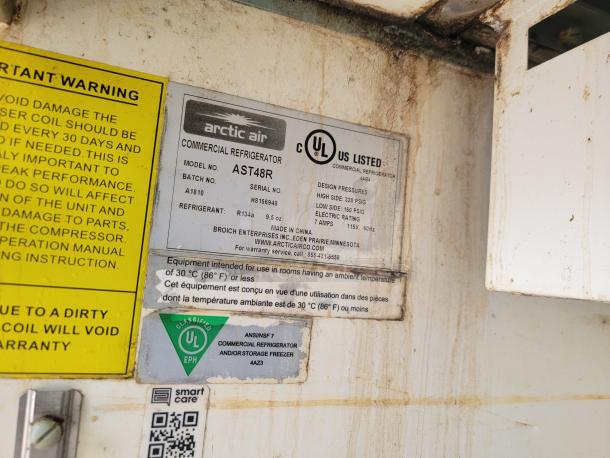 Arctic Air commercial refrigerator label, model AST48R, indicates design pressures, refrigerant type R134a. Visible dirt present.