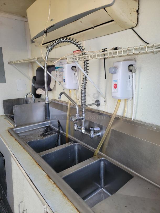 2019 Diamond Cargo 24' Mobile Kitchen interior with triple sink setup, dual faucets, and visible water heaters; needs cleaning.