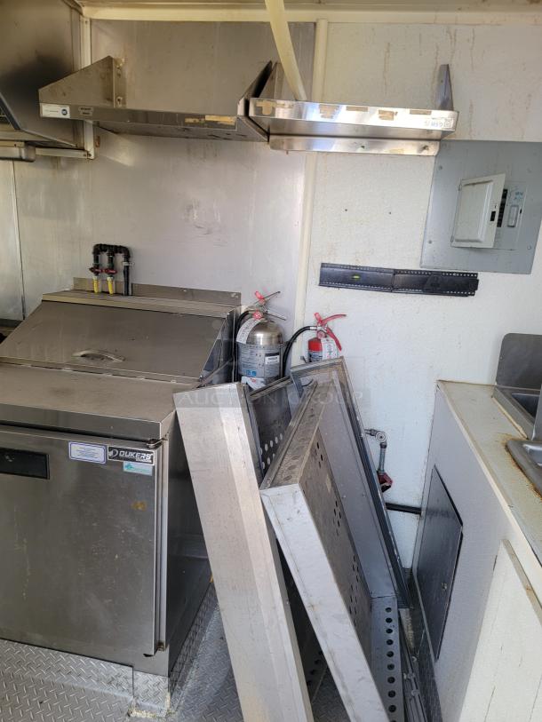 2019 Diamond Cargo mobile kitchen interior, featuring Dukers refrigeration, shelving, and fire extinguishers. Needs cleaning and minor repairs.