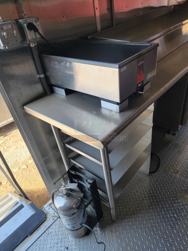 Interior of 2022 Rock Solid Cargo 28' mobile kitchen. Features Cayenne countertop appliance, shelves, power outlets, and an extinguisher.