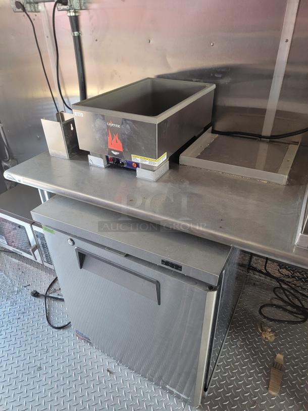 2022 Rock Solid Cargo mobile kitchen interior with stainless steel counter, Cayenne warmer, fridge, and metal flooring.