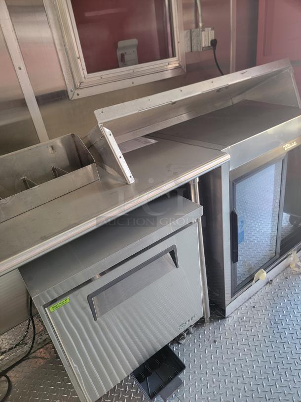 2022 Rock Solid Cargo 28' mobile kitchen interior with stainless steel surfaces, commercial fridge, and electrical panel.