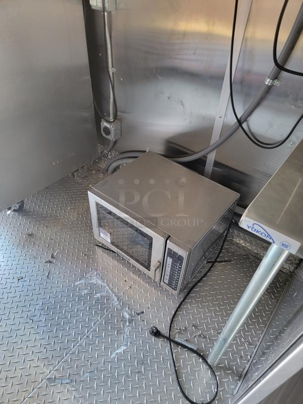 Interior view of 2022 Rock Solid Cargo 28' mobile kitchen with stainless steel microwave on diamond plate flooring.