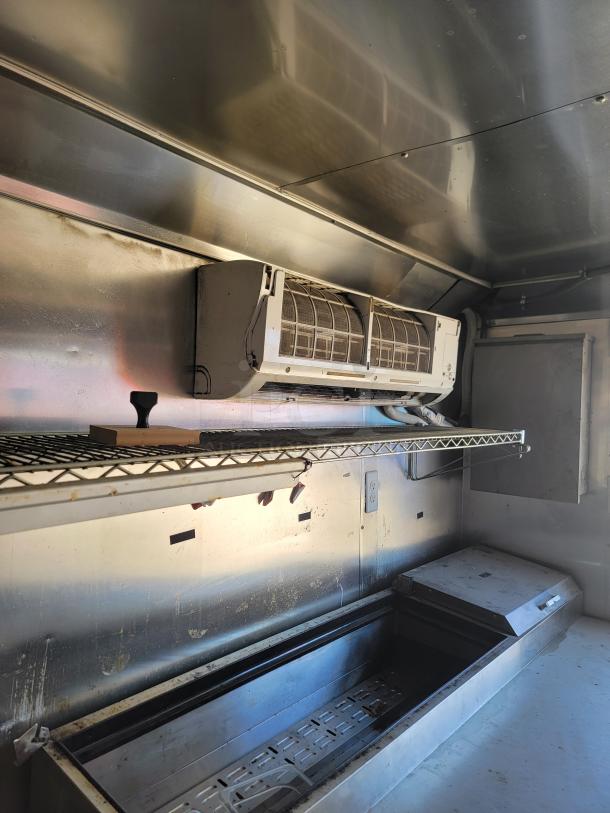 Interior view of a 2019 Peach Cargo mobile kitchen. Features metal shelving, an A/C unit, and prep area, showcasing rugged construction.