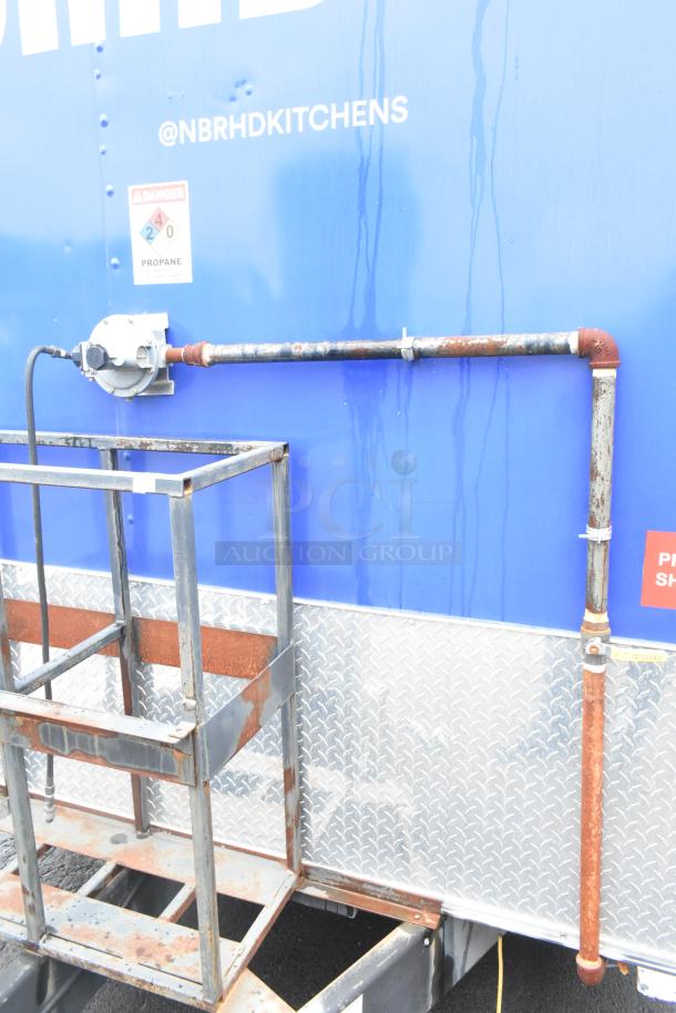 Exterior view of a 2021 Rock Solid Cargo food trailer with propane setup. Features diamond plate siding, @NBRHDKITCHENS branding, and safety label.