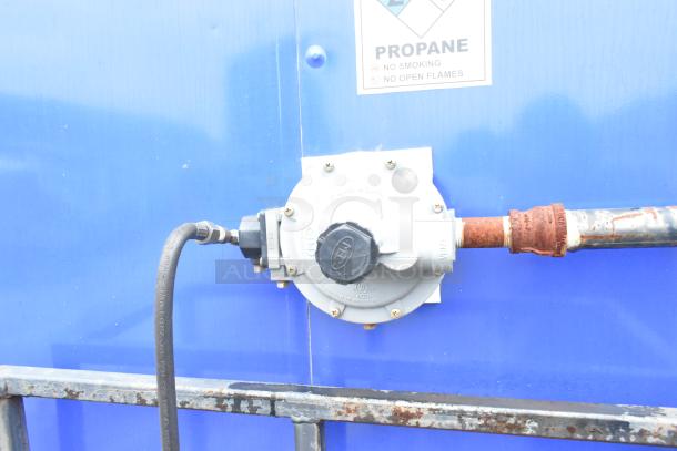 Propane connection on blue exterior of Rock Solid Cargo trailer with safety warning label.