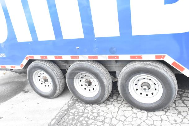Blue Rock Solid Cargo trailer, showing side view of three wheels and red reflective trim.