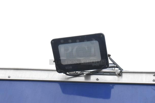 LED floodlight on the exterior of a blue mobile kitchen trailer, marked 50W and IP66.