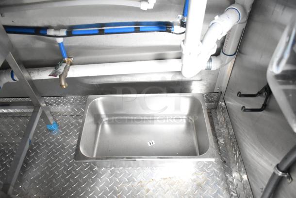 Interior view of a Rock Solid Cargo 24' fast food trailer showing plumbing and sink setup on metal flooring.