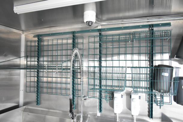 Interior of a 2021 Rock Solid Cargo 24' mobile kitchen trailer, featuring wire shelving, spring faucet, and commercial equipment.