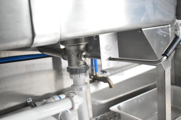 Under-sink plumbing of brand new Rock Solid Cargo mobile kitchen. Stainless steel fixtures and white PVC piping visible.