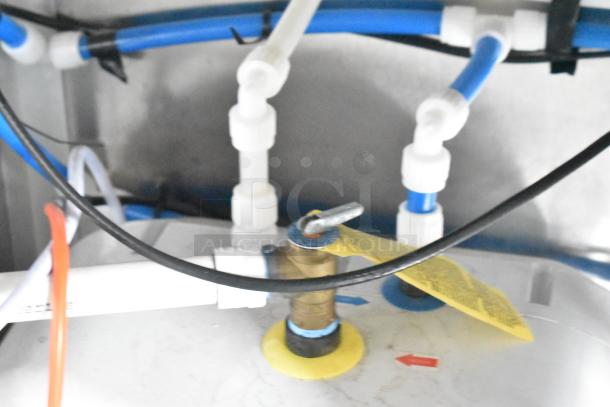 Close-up of plumbing connections inside a Rock Solid Cargo mobile kitchen trailer, featuring blue and white pipes, a valve, and tags.