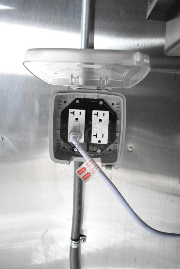 Electrical outlet with dual sockets in a brand new Rock Solid Cargo mobile kitchen trailer, featuring a clear protective cover.