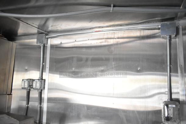 Interior view of a brand new 2021 Rock Solid Cargo 24' mobile kitchen trailer with shiny metal walls and multiple electrical outlets.