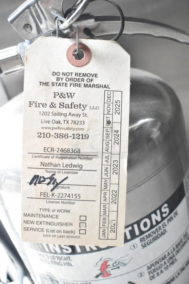 Alt text: Fire extinguisher with P&W Fire & Safety service tag, expiration 2025, attached to Rock Solid Cargo mobile kitchen trailer.