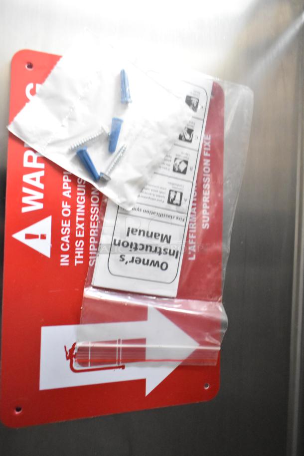 Red warning sign and owner's manual for fire suppression system with screws and wall anchors on a Rock Solid Cargo mobile kitchen.