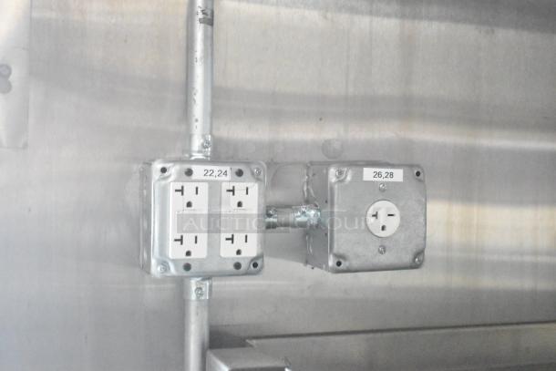 Electrical outlets in a Rock Solid Cargo food trailer, labeled 22, 24 and 26, 28, next to stainless steel wall surface.