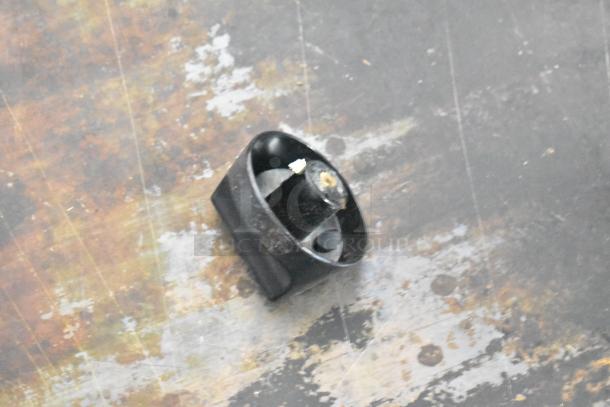 A metal knob rests on a worn and discolored flat surface. The knob appears black and cylindrical with a hollow interior. The surrounding surface displays rust and wear marks, indicating frequent usage or exposure to elements.