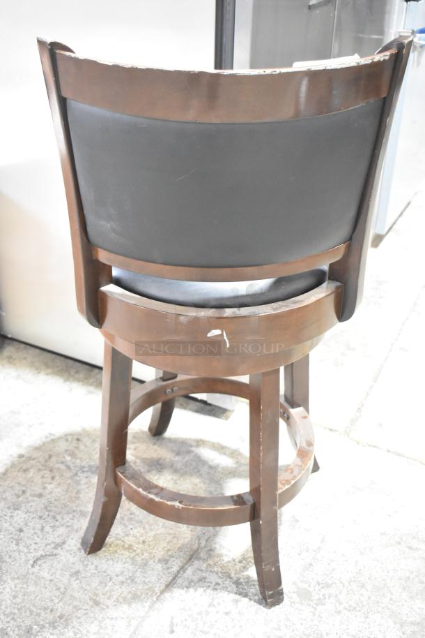 Bar height chair with wood pattern finish and black backrest. Visible wear on edges and legs. Swivel base feature.