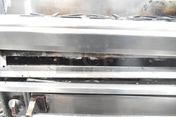 Jade Range gas-powered 6 burner, 2 tier range with oven and backsplash on commercial casters. Shows wear and rust.