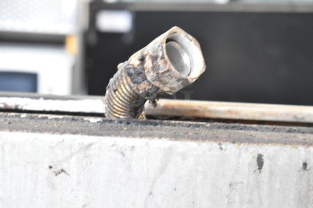 A close-up of a pipe on a Jade Range commercial gas-powered 6-burner range, showing signs of wear and rust.