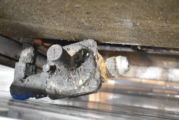 Close-up of a worn component from a Jade Range commercial gas burner, showing significant rust and grime buildup.