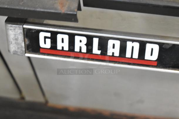 Garland gas-powered griddle and 6-burner range with 2 ovens, featuring a back splash. Brand tag visible. Good condition.