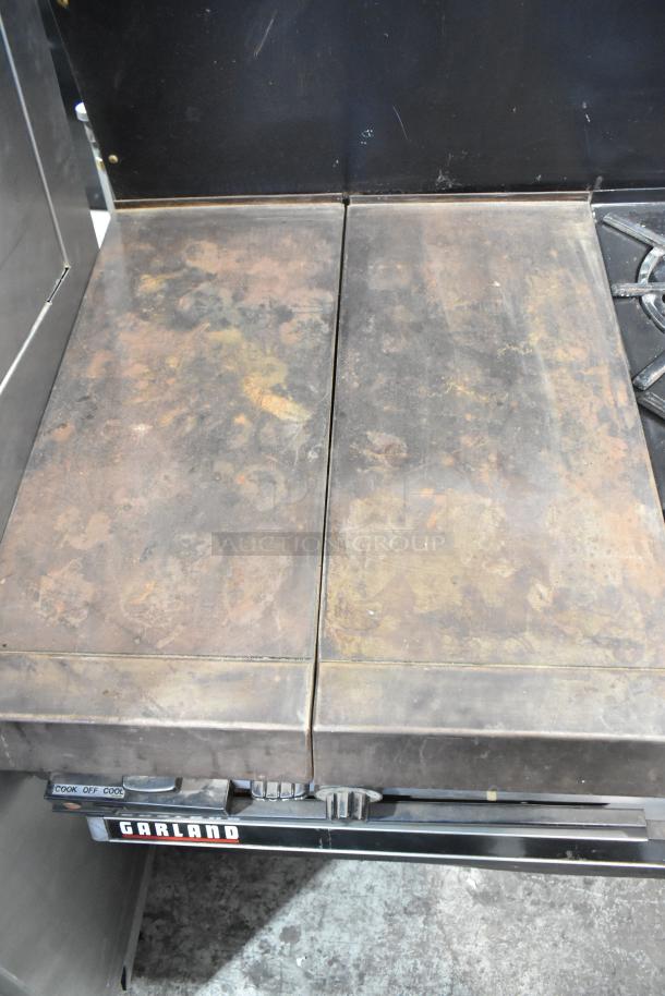 Garland gas-powered flat top griddle with 6 burner range, 2 ovens, and backsplash. Used condition with visible wear.