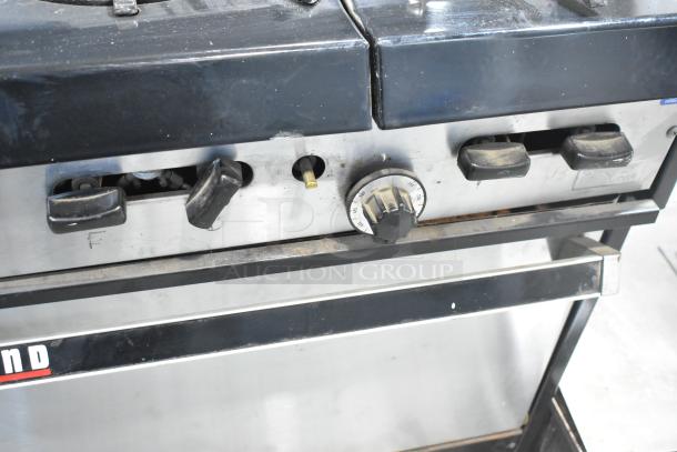 Garland commercial gas griddle with 6-burner range, 2 ovens, and backsplash. Control knobs and surfaces show wear.