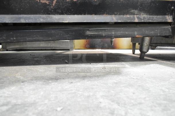 Garland commercial gas griddle with 6 burner range, 2 ovens, and back splash. Visible wear and signs of use on lower frame.