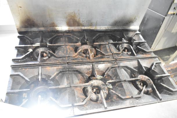 American Range 6-burner gas stove with oven, overshelf, backsplash, on commercial casters. Visible wear and stains.