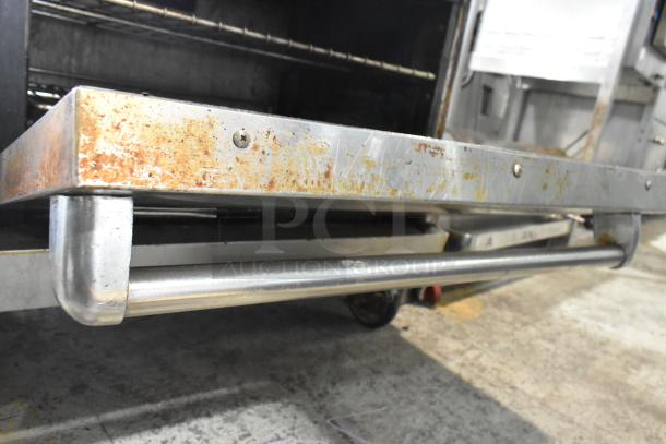 American Range 6 burner gas stove with oven, over shelf, backsplash. Visible wear and rust on commercial casters.