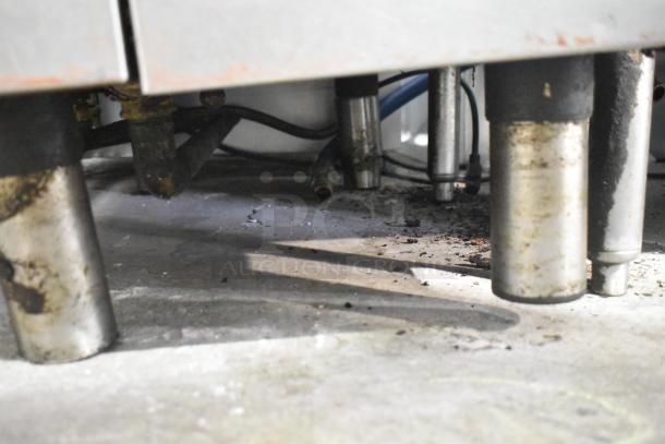 Commercial floor style pasta cooker base with visible pipes and wiring, showing signs of wear. No visible tags or labels.