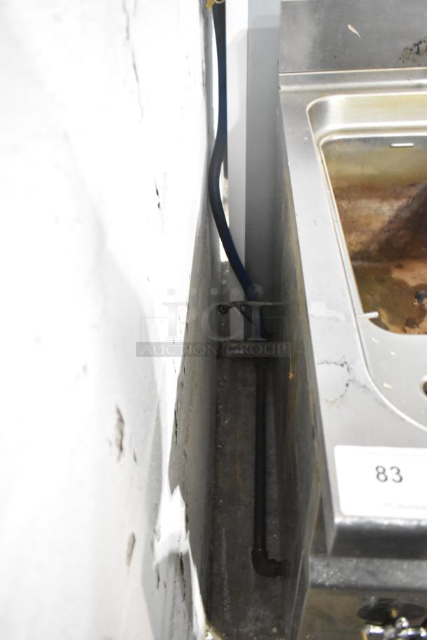 Commercial floor-style pasta cooker, stainless steel, visible piping, signs of wear, auction label number 83 attached.