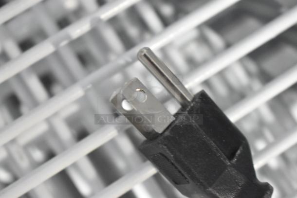 Close-up of plug on True TSCI-600R-G-PH cooler merchandiser, showing metal prongs, set on metal grid surface.