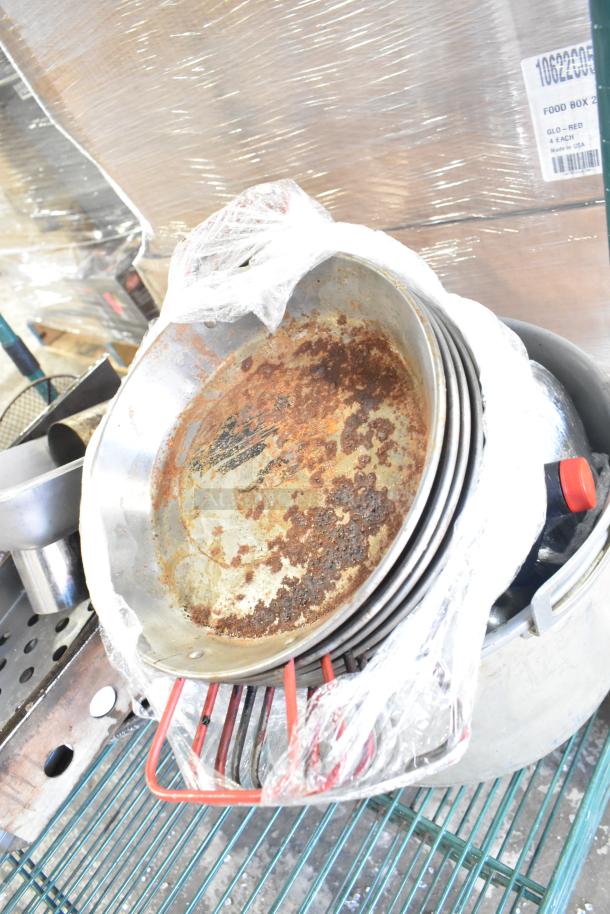 Tier lot with skillets, bowls, coffee pot, and metal pot, showing signs of rust and wear, wrapped in plastic on a metal rack.
