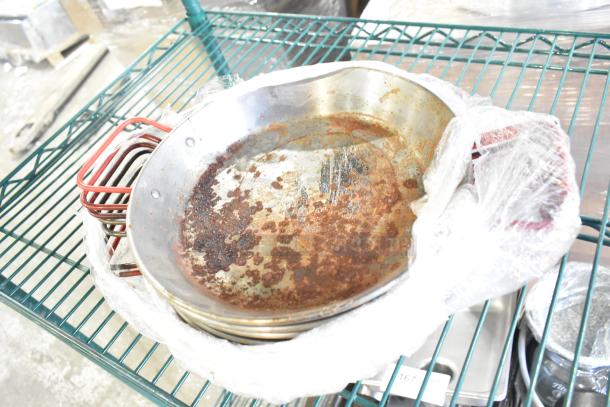 Assorted kitchen items with skillets, bowls, coffee pot, metal pot on a shelf. Skillets show rust and wear. Wrapped in plastic.