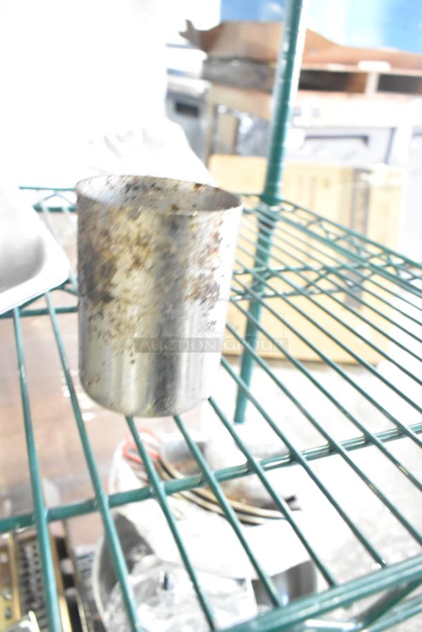 Tiered auction lot with metal pot, visibly rusted, on green wire shelf. Includes skillets, bowls, coffee pot. Various conditions.