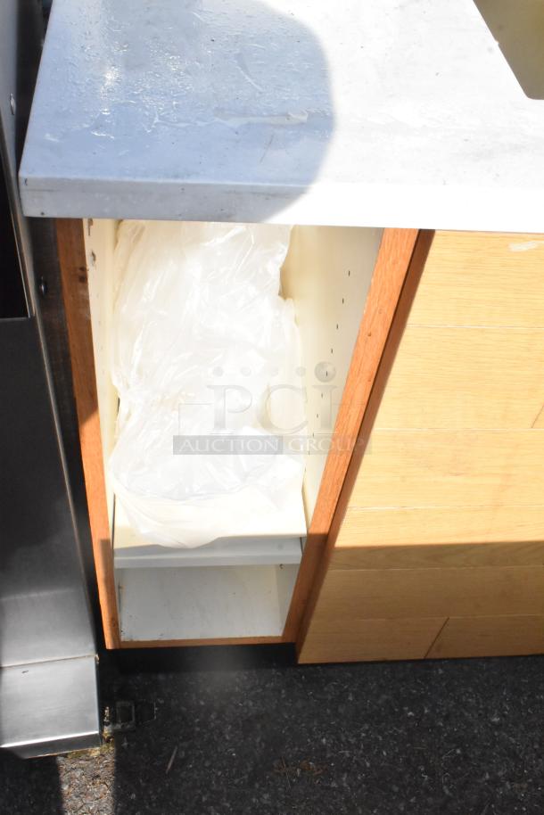 Wooden trash can shell, white interior, under marble counter, includes plastic bag lining, showing minor wear.