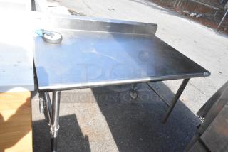 Stainless steel commercial table with backsplash, caster wheels, and sturdy legs, showing slight surface wear.