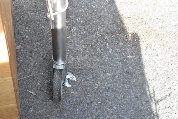 Stainless steel leg of a commercial table with a caster wheel, marked "China," on an asphalt surface.