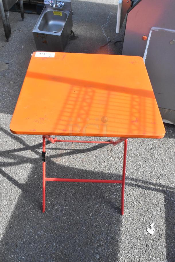 Orange folding table with red metal legs, in used condition. Price tag reads "6 times your bid."