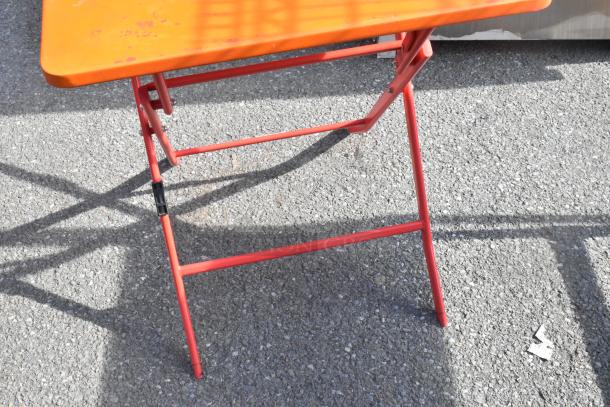 Set of six orange folding tables with red legs, outdoor use, light wear, durable build, ready for versatile applications.